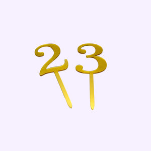 Two gold number cake toppers, '2' and '3', on a white background.